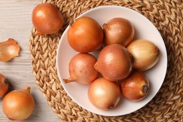 Many ripe onions on wooden table, flat lay