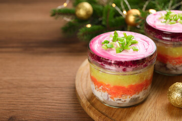 Glass jars with herring under fur coat and Christmas decor on wooden table, space for text. Traditional Russian salad