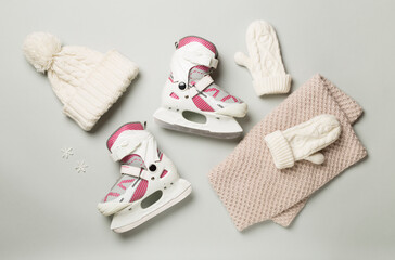 Ice skates and knitted hat on color background, top view