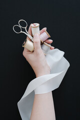 Sewing supplies and silver scissors and a natural white silk ribbon in woman hand against black...
