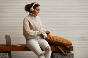 A young afro american woman sitting on a wooden bench in an urban environment with wireless...