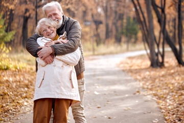 Fototapeta premium Joyful Friendly Senior Elderly Couple In Coats Enjoy The Walk Together, Hugging, Laughing. Caucasian European Married Man And Woman In Love, During Autumn Season. Happiness, Lifestyle Concept