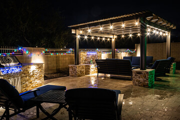 A resort style backyard at night with a waterfall, pergola, and a firepit at night. - Powered by Adobe