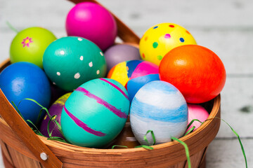 Obraz na płótnie Canvas Basket with painted colorful easter eggs on wooden table