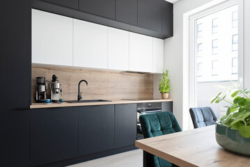 Interior of kitchen with modern black kitchen furniture, table and chairs and window. 