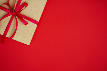 Flat lay. Valentine's Day. On the right is a box, wrapped in craft paper and a red ribbon, next to red and pink hearts. Red background.