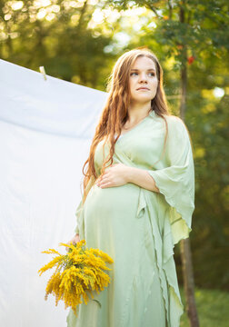 Pregnant woman with big belly, yellow Goldenrod Solidago flowers in hands. White female wears dress.Magic happy pregnancy. Childbirth preparations,emotional connection with baby. Baby shower Vertical