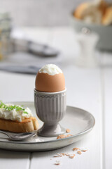 Fresh soft boiled egg in cup and sandwich on white wooden table