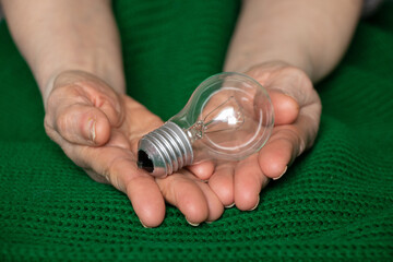 An incandescent lamp lies in the hands of an old woman on a green knitted fabric, without light