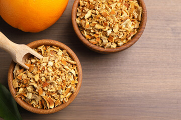 Bowls of dried orange zest seasoning and fresh fruit on wooden table, flat lay. Space for text