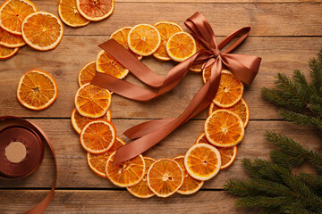 Decorative wreath made with dry oranges, ribbon and fir branches on wooden table, flat lay