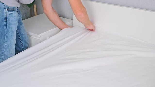 A man makes his cozy bed with fresh bright white bed linen. Making the bed with fresh bed linen by man. The day of the change of bedclothes.