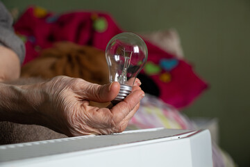 An incandescent lamp in the hands of an old woman vozli batteries in the apartment, people without...