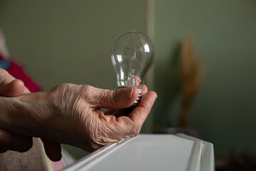 An incandescent lamp in the hands of an old woman vozli batteries in the apartment, people without...