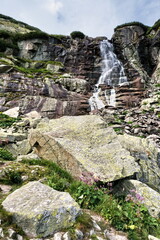 Waterfall with rocks, green grass and blue sky. Waterfall in High Tatra mountains. Beautiful Slovak nature. Hiking, adventure and nature concept. © stefanbalaz