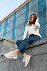 Young brunette woman posing for photo on modern city background. Beautiful student girl on summer city street