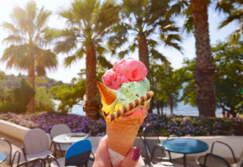 Woman hand hold ice cream  in waffle  , background of panoramic view of beach with sea and coconut palm trees in Porec, Croatia