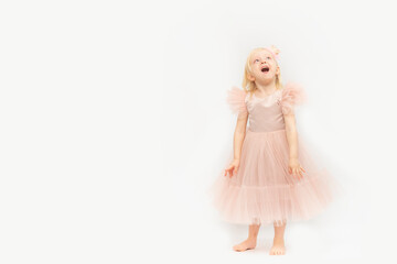 Laughing girl in festive pink dress stands and look up. Blonde Princess isolated on white background. Space for text