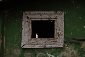 Three candles stand on a broken window of an old residential building, view from the street through the window, the light of a candle in a window in Ukraine, people without light at home 2023