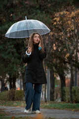 Woman with transparent umbrella walking in park in fall and talkin to phone. Young beautiful woman using smartphone under umbrella.