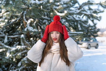 Portrait of beautiful young brunette woman in knitted red hat and mittens in winter park. Little Red Riding Hood.