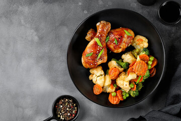 Roasted Baked chicken legs drumsticks with vegetables on black plate on dark background. Meal, dinner diet concept, diet. Top view, copy space.