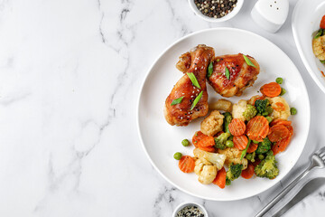 Roasted Baked chicken legs drumsticks with vegetables on white plate on marble table. Meal, dinner...