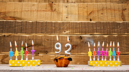 Muffin with a burning candle background for the anniversary on a beautiful wooden background. Postcard with letters of candles with congratulations for the holiday before the birthday.  Copy space 92