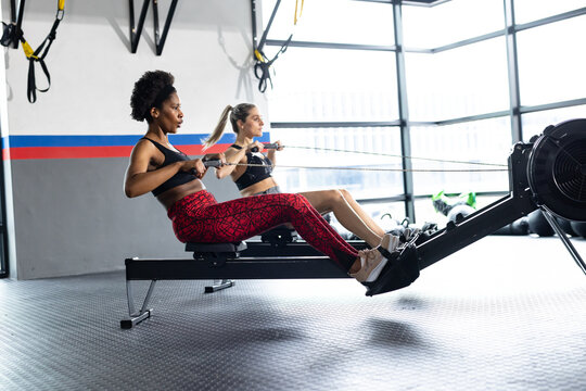 Diverse fit women exercising and using rowing machines at gym
