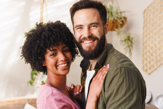 Close-up portrait of cheerful biracial young couple hugging against white wall, copy space