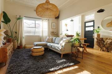 Rattan pendant light hanging over sofa, ottoman stool, houseplants and carpet in living room
