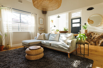 Rattan pendant light hanging over sofa, ottoman stool, houseplants and carpet in clean living room