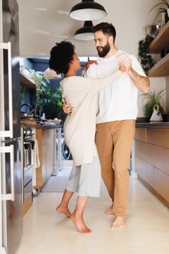 Full length of biracial young couple dancing romantically in kitchen at night, copy space