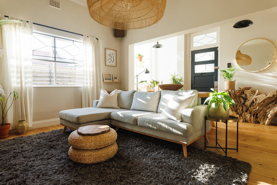 Rattan pendant light hanging over sofa, ottoman stool, houseplants and carpet in clean living room