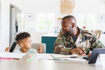 Happy african american father wearing military uniform and his son working and doing homework