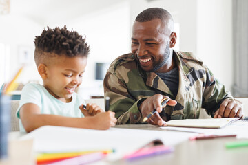 Happy african american father wearing military uniform and his son working and doing homework