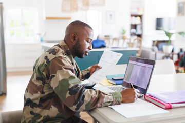 Happy african american man wearing military uniform sitting at table and working