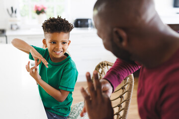 Happy african american father and son at table, talking in sign language