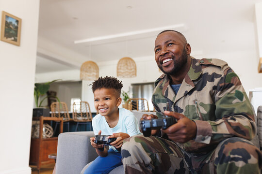 Happy african american father wearing military uniform and his son playing video games