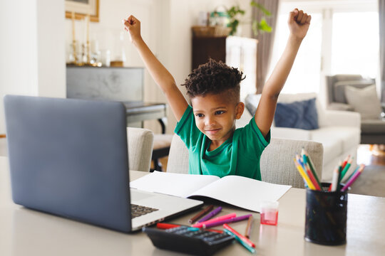 Happy african american boy sitting at table, using laptop for online lesson
