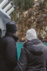 married couple viewing scenic frozen waterfall on rocky cliff of Kenai over Resurrection Bay in Seward Alaska in winter, vertical framing