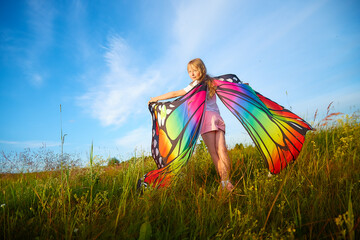 Pretty blonde girl with bright butterfly wings having fun in meadow on natural landscape with grass...