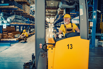 Senior worker driving electric forklift at workplace - obrazy, fototapety, plakaty
