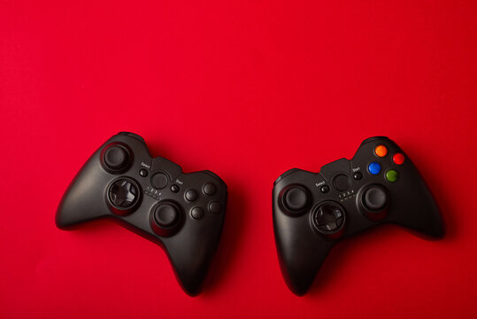 Black Video Game Controller, Joystick For Game Console Isolated On Red Background. Gamer Control Device Close-up