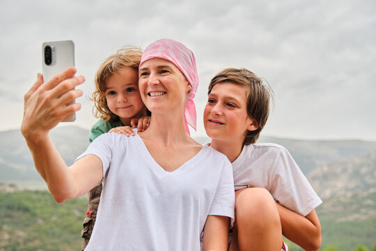 A woman with cancer taking a selfie with her family in the mountains.
