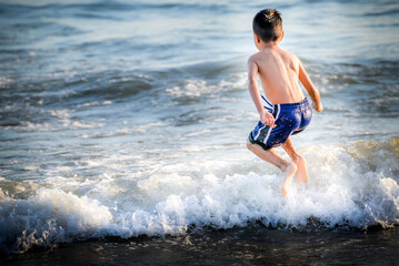 Fototapeta premium Young boy jumps over a wave and into the Pacific Ocean in Santa Monica, California