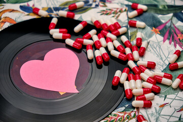 Vinyl record with a pink heart and a bunch of pills, on top of a table with a tropical pattern.