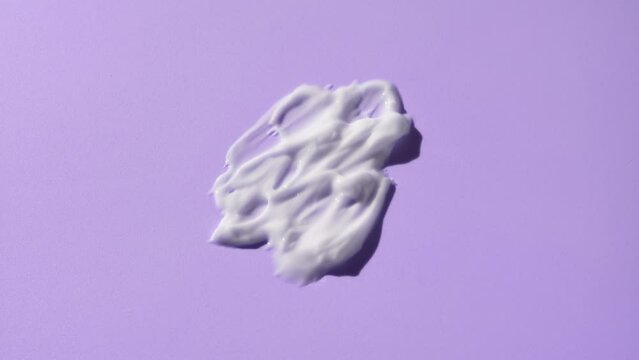 Macro crane shot of white cosmetic lotion smears on purple background | White cosmetic lotion commercial