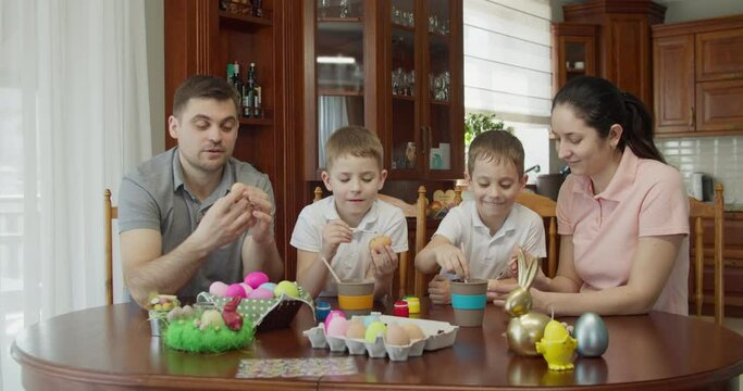 a happy family sits at a table and paints Easter eggs. the boy gives five to his mother