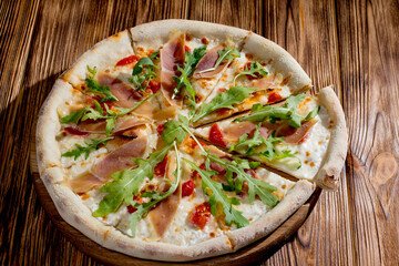 Pizza with jamon and prosciutto, mozzarella, cherry tomatoes, arugula and parmesan on a wood background. Italian cuisine.